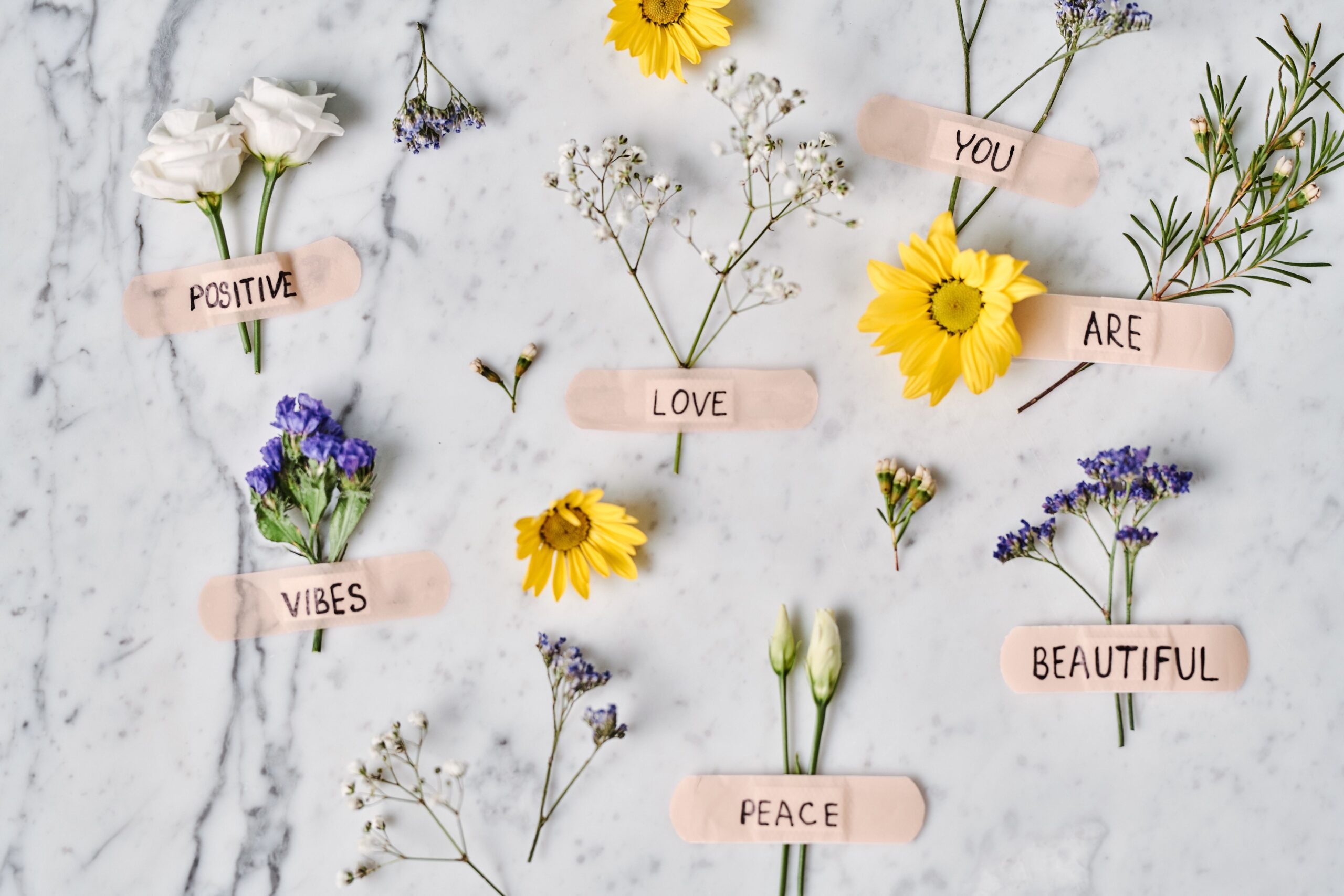 Floral flat lay with positive words on band-aids over a marble surface, promoting peace and love.